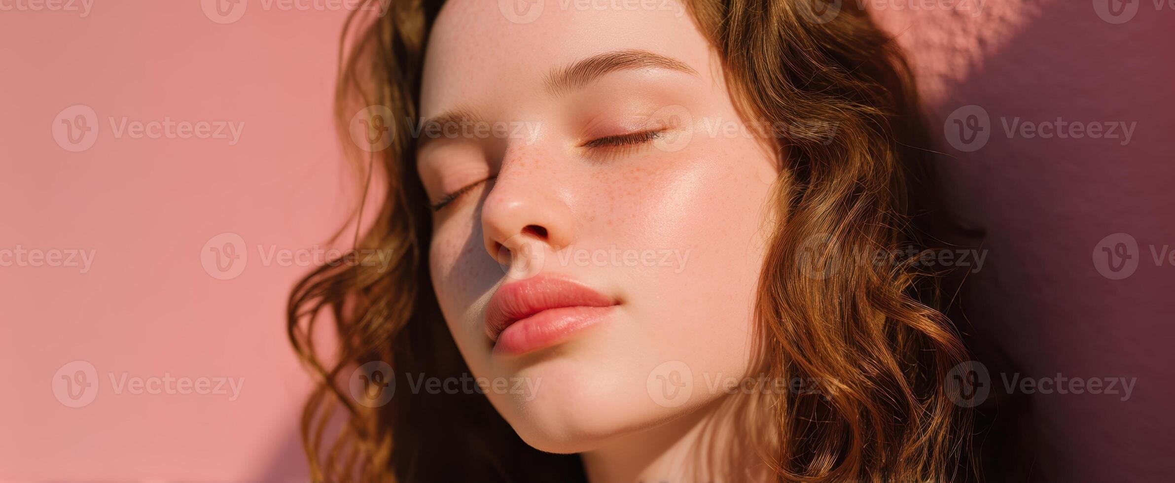 The serene beauty of a young woman basking in soft sunlight against a pink backdrop. photo