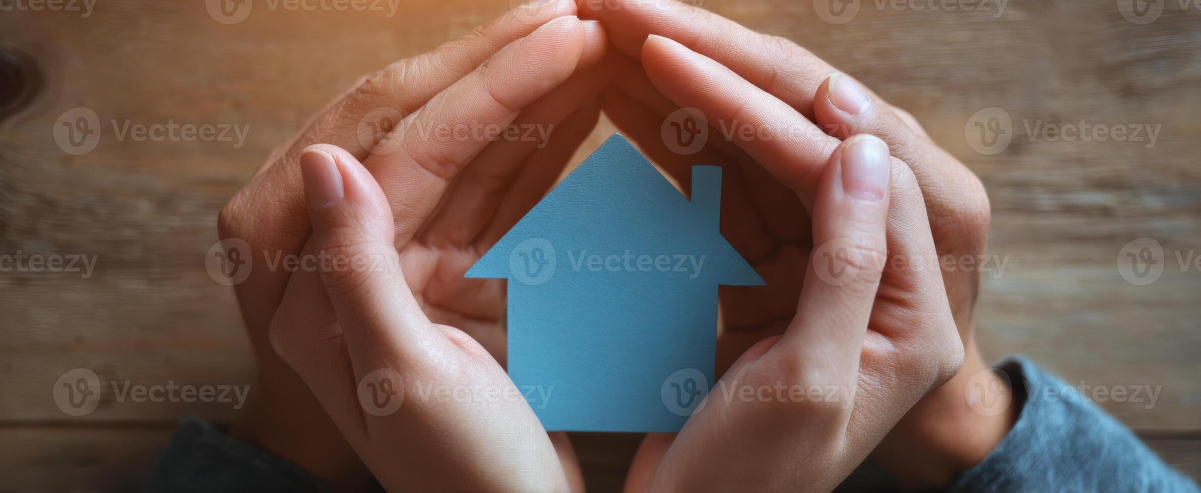 The hands protecting a blue house model symbolizing home and safety. photo