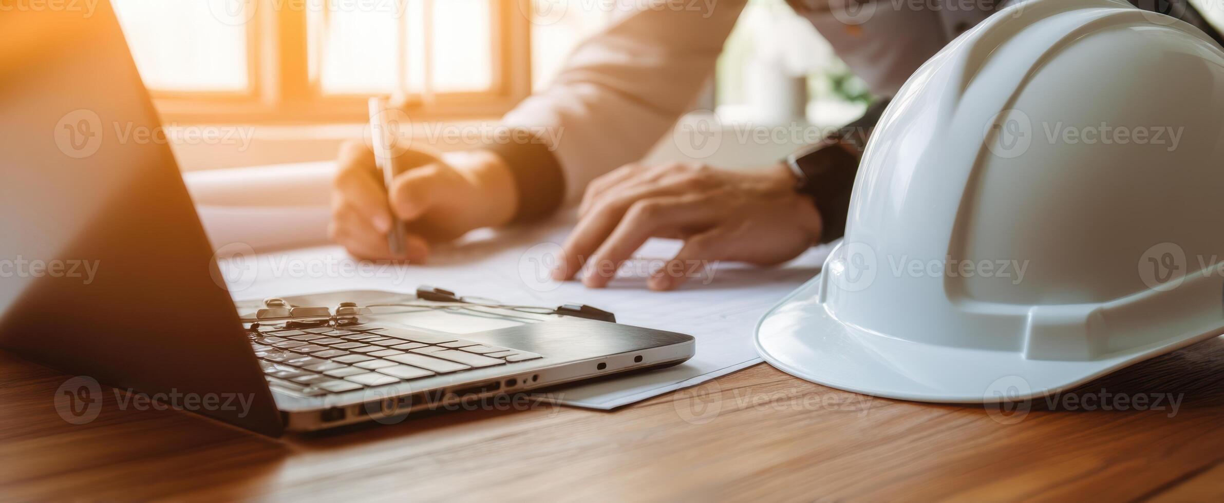 The engineer writing plans at a modern workspace with a laptop and hard hat. photo