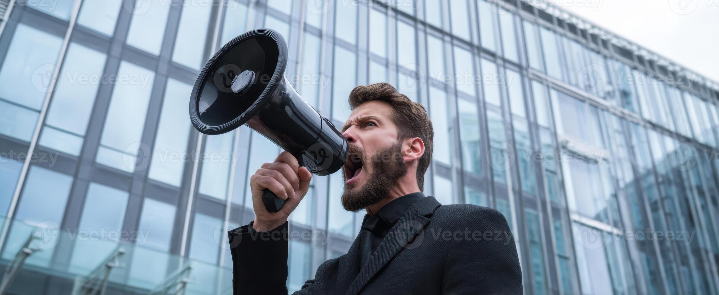 The man passionately shouting into a megaphone outside a modern glass building. photo