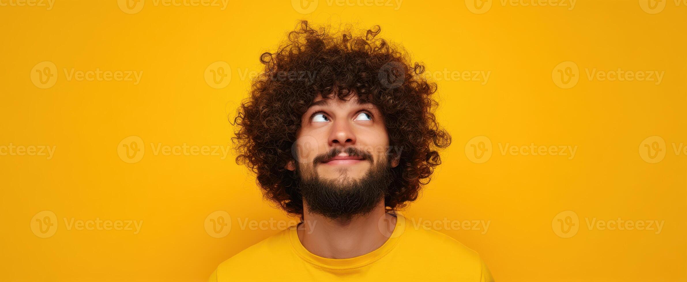 The young man with curly hair enjoying a moment of imagination against a yellow backdrop. photo