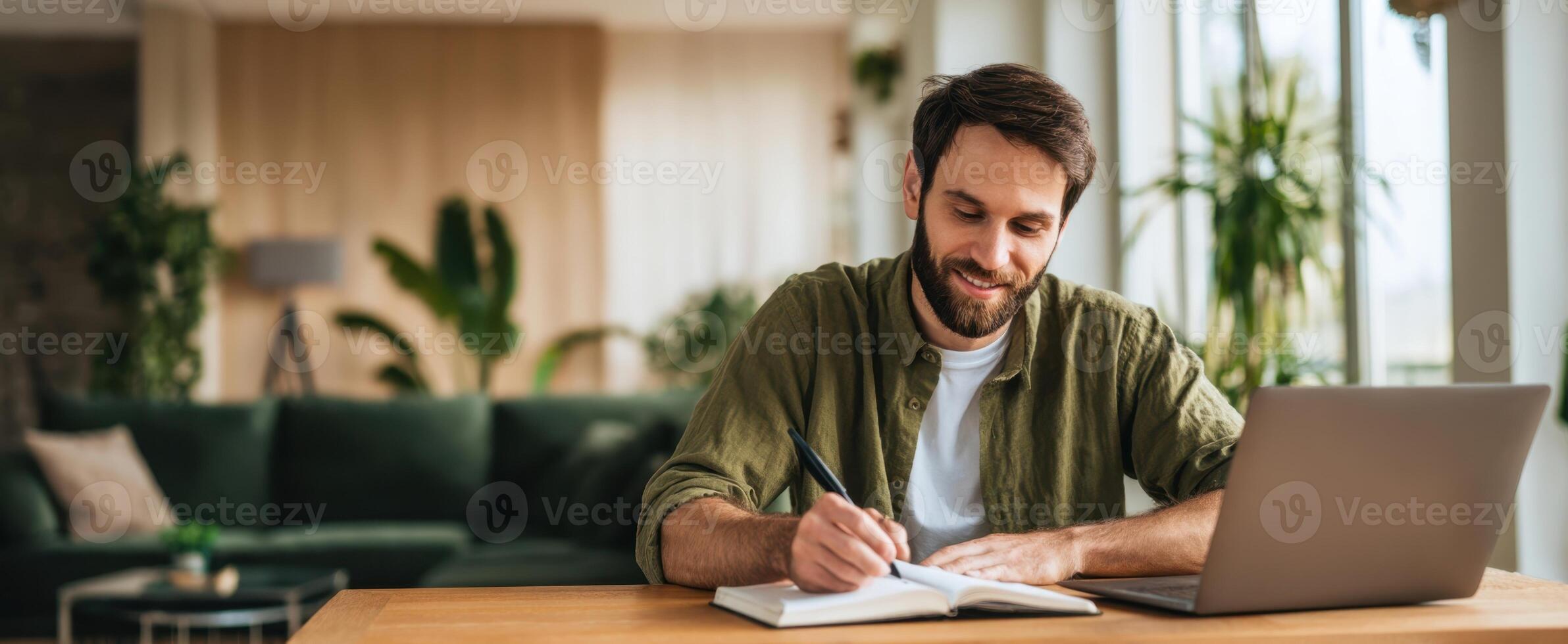 The man writing in notebook while sitting at modern home workspace. photo