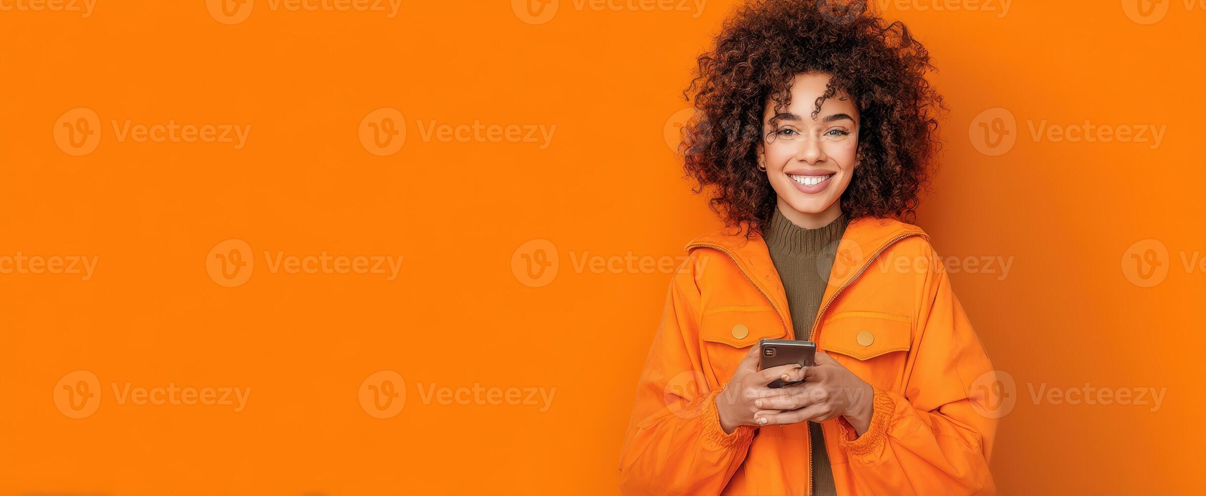 The smiling woman wearing an orange jacket using a smartphone against a vivid backdrop. photo