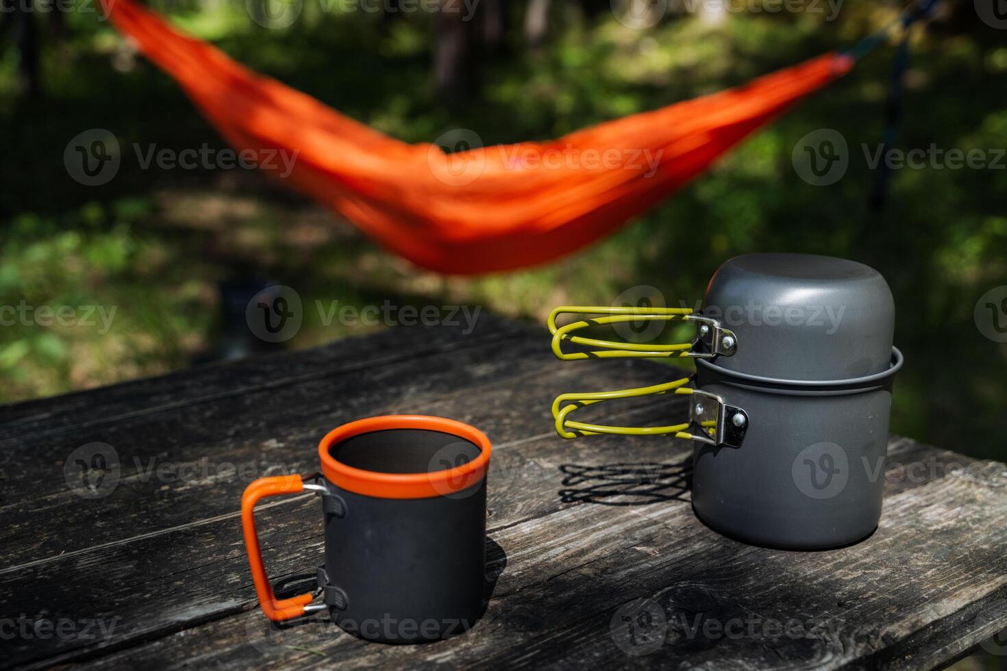 A comfortable hammock is gently swaying, suspended above a sturdy wooden table that has two mugs and various pots neatly arranged on its surface, ready for use or display photo