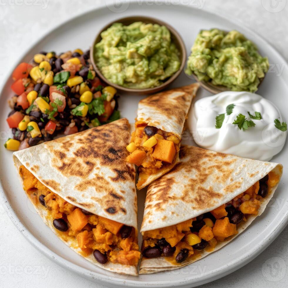 A plate of sweet potato and black bean quesadillas, filled with a flavorful mixture of sweet potatoes, black beans, corn, spices, cheese, and a hint of smoky chipotle, served with guacamole, salsa, photo