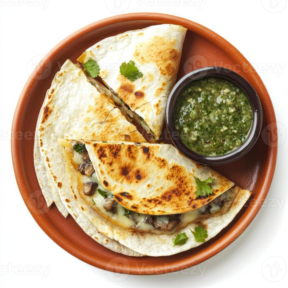 A plate of cheesy quesadillas, filled with melted Oaxaca cheese, mushrooms, and epazote, grilled until golden brown and served with a side of salsa verde, arranged on a terracotta plate. isolated on photo