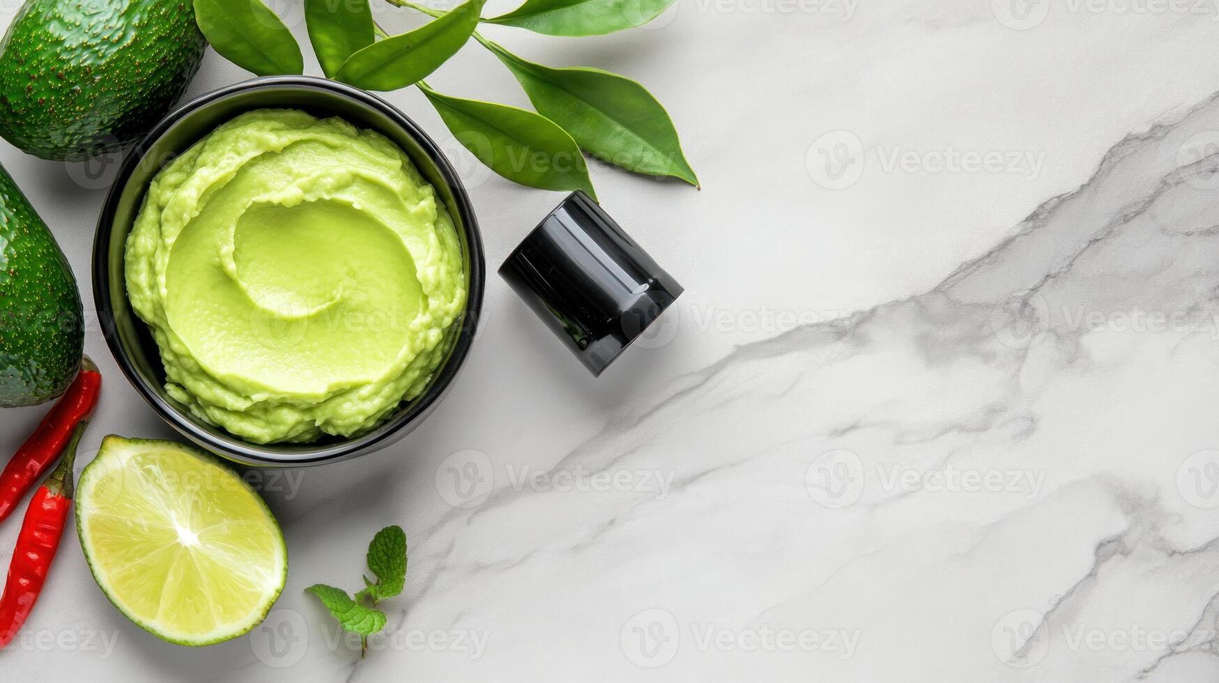 Avocado dip with lime and chili pepper on a marble table with decorative green leaves, for a healthy meal photo