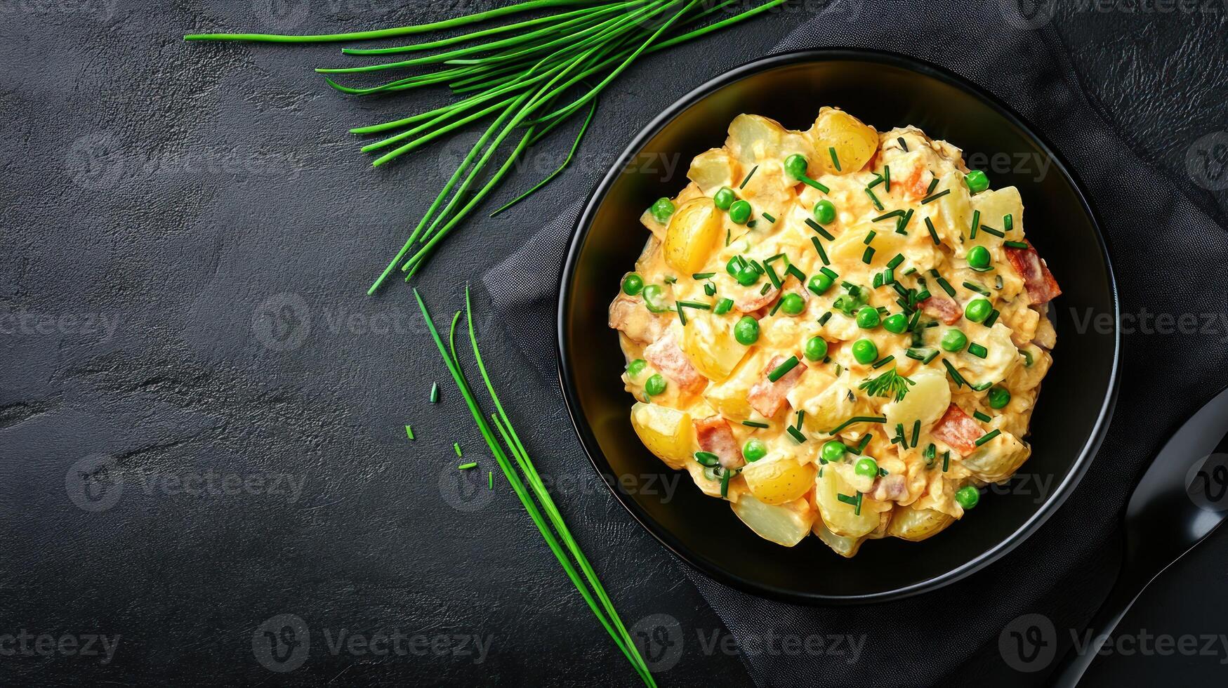 Bowl of potato salad with peas and chives on black table setting, ready for lunch photo