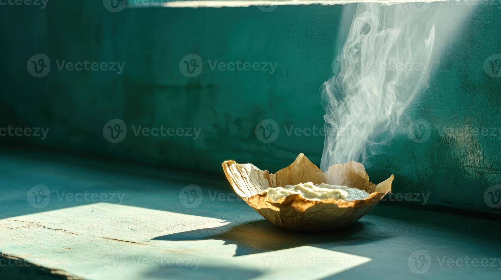 Burning incense in paper bowl sits on windowsill sunlight shines on textured turquoise wall photo