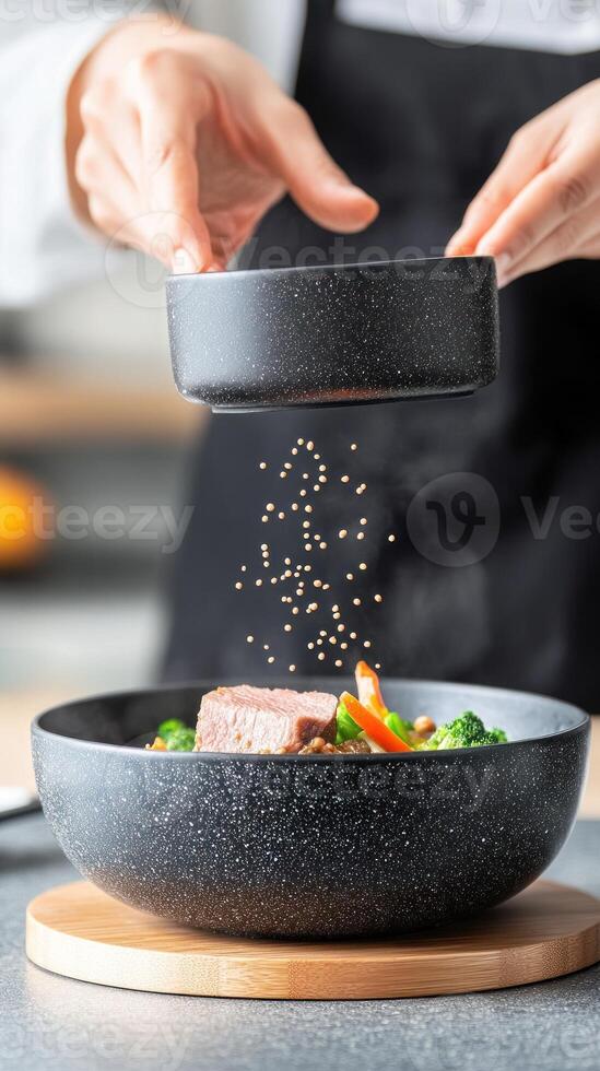 Chef adds seasoning to bowl of food in kitchen blurred background. Food preparation photo