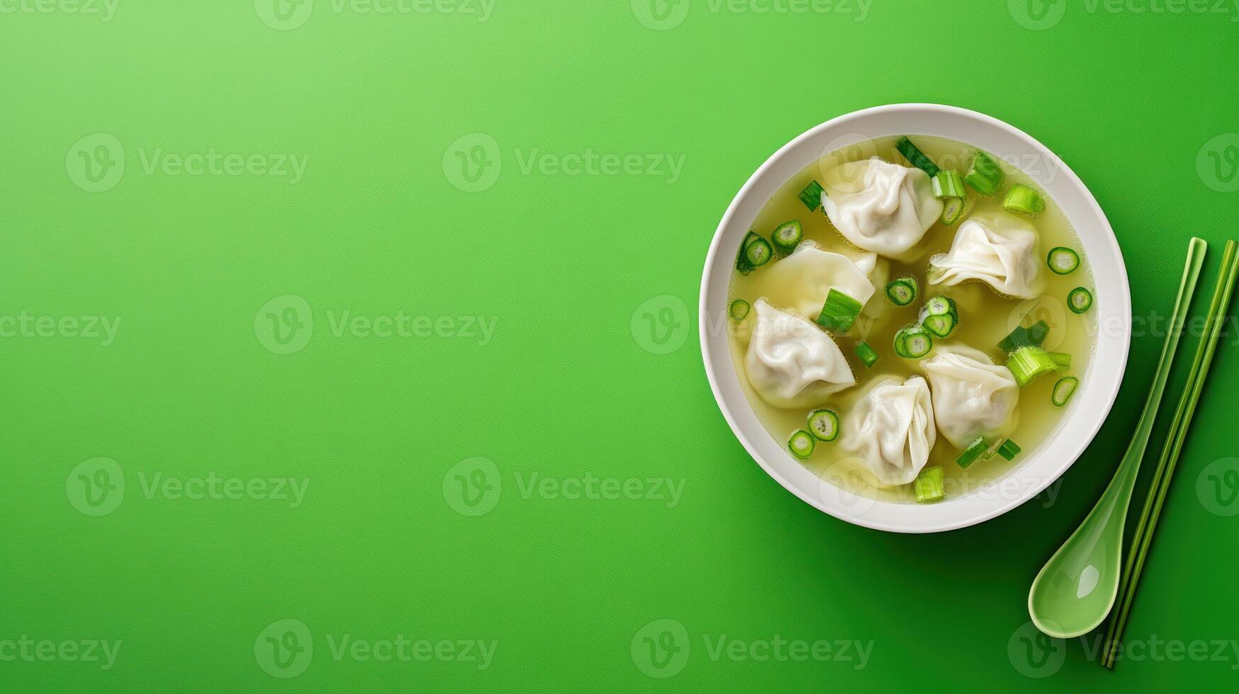 Dumpling soup served in a bowl. Chopsticks and spoon sit nearby on a green table for a delicious meal photo