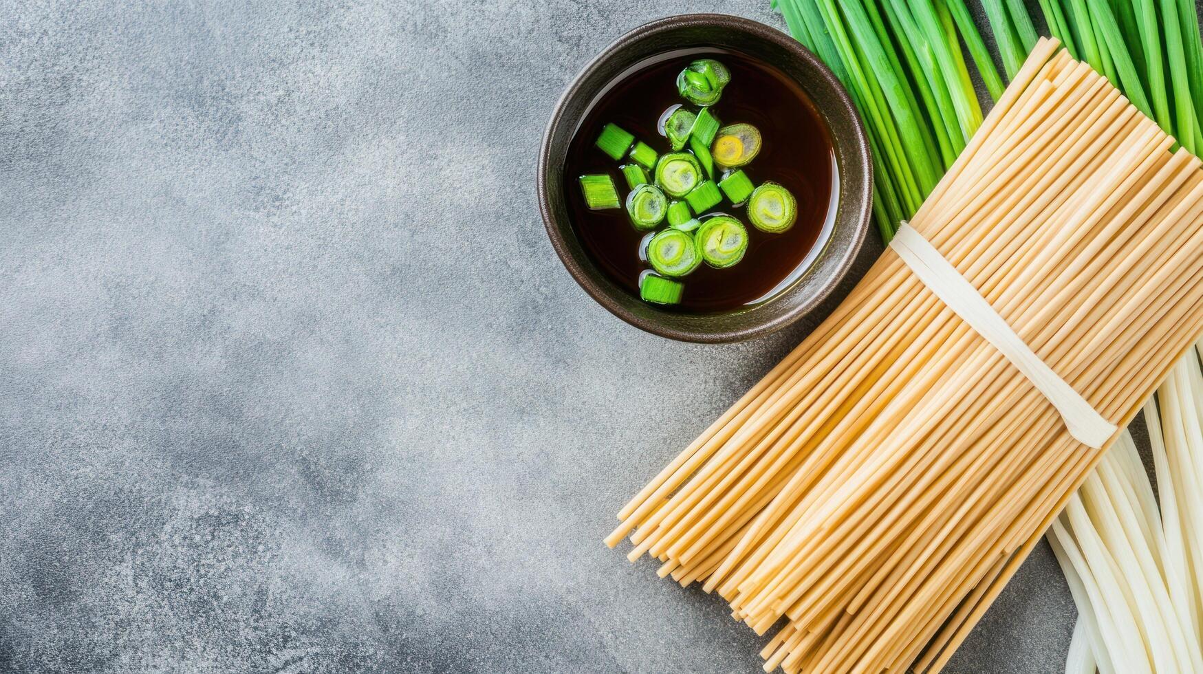 Noodles ready to cook, with broth and green onion, on grey textured table, for a food blog post photo