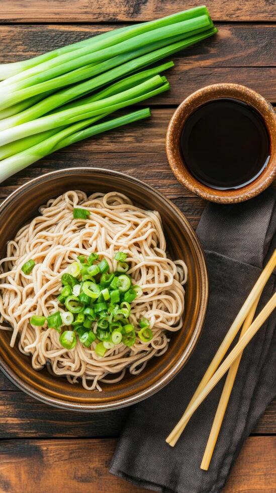 Noodles topped w scallions, a soy sauce and chopsticks on wooden table. Food blog, ad or recipes photo