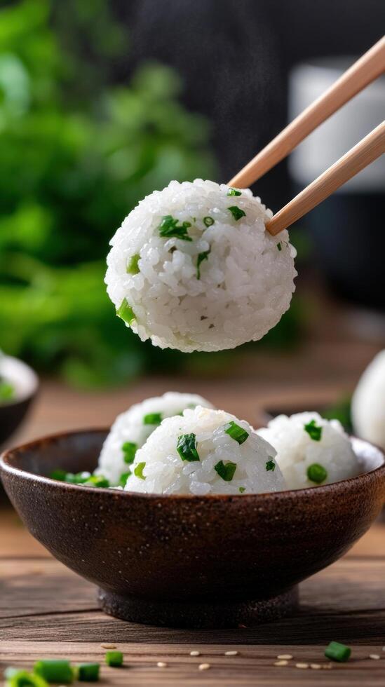 Rice ball with greens held by chopsticks on a wooden table against greenery. Food photo