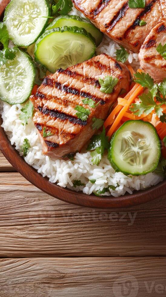 Salmon bowl with rice, cucumber, and carrots, served on a wooden table, ready to eat photo