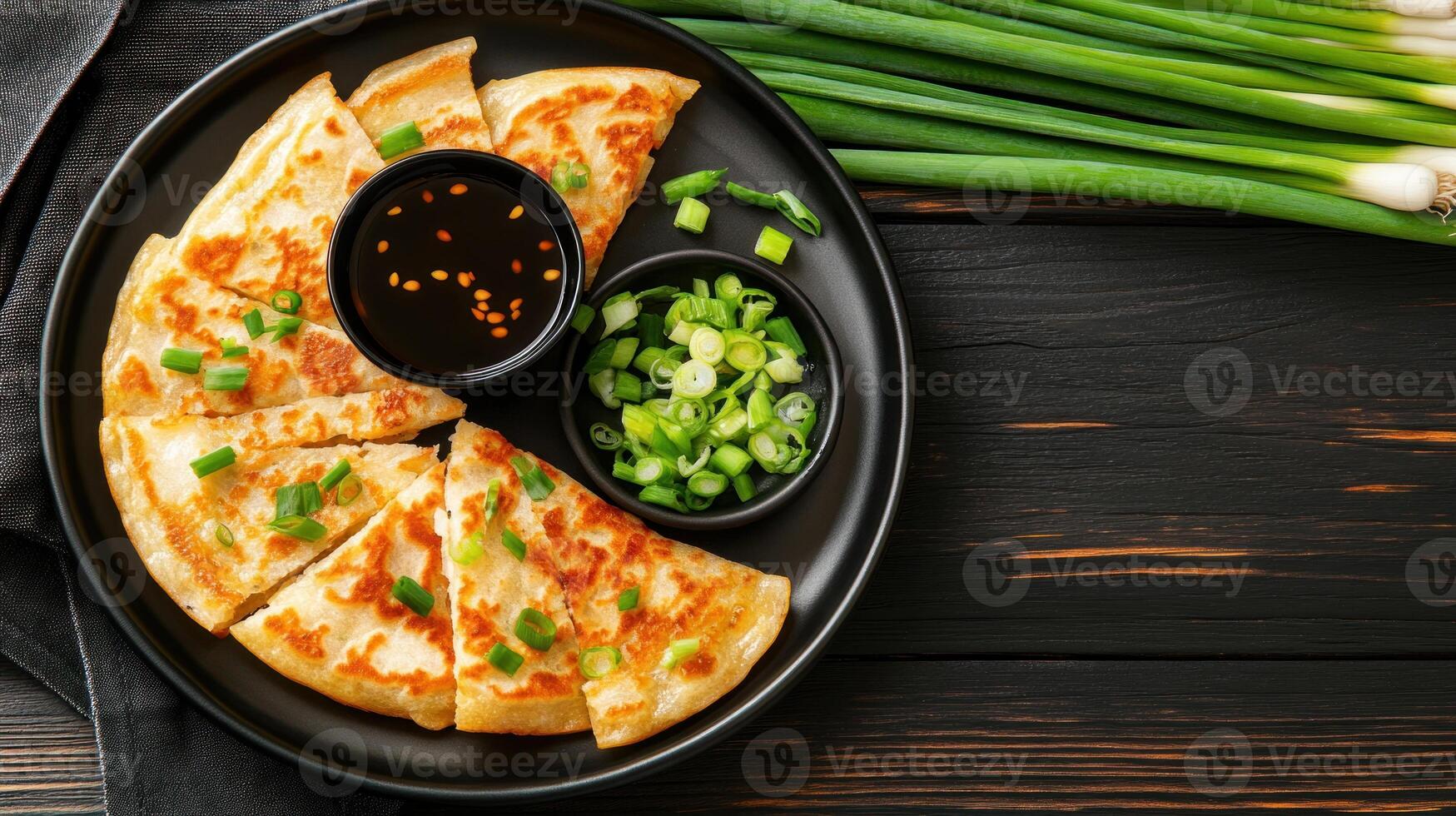 Scallion pancake wedges on a dark plate, with dark dipping sauce and onions in the background, for food blog photo