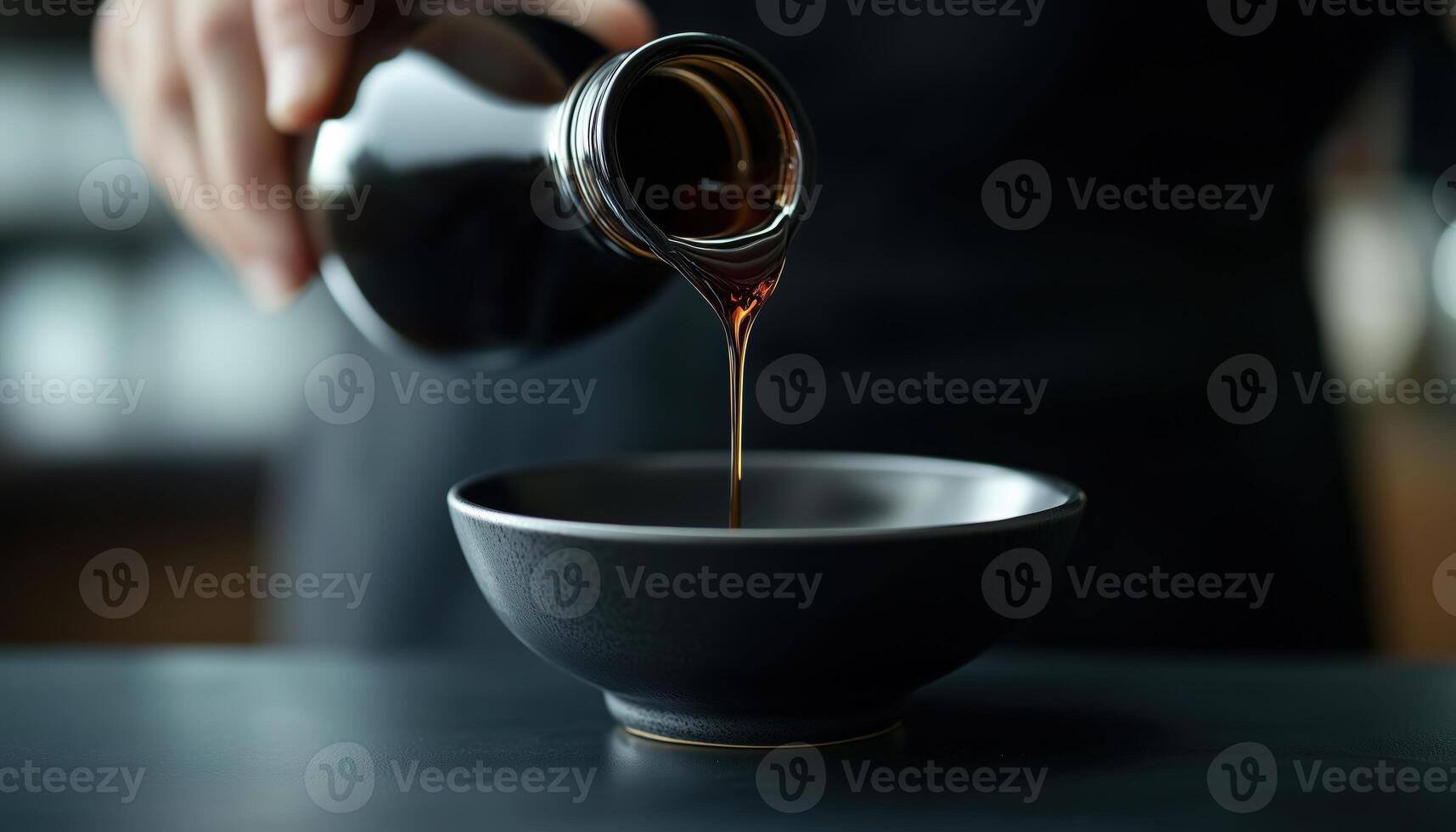 Close Up Shot Of Delicious Soy Sauce Being Poured From Bottle Into Bowl On Black Table, Showing The Tasty Pouring Process photo