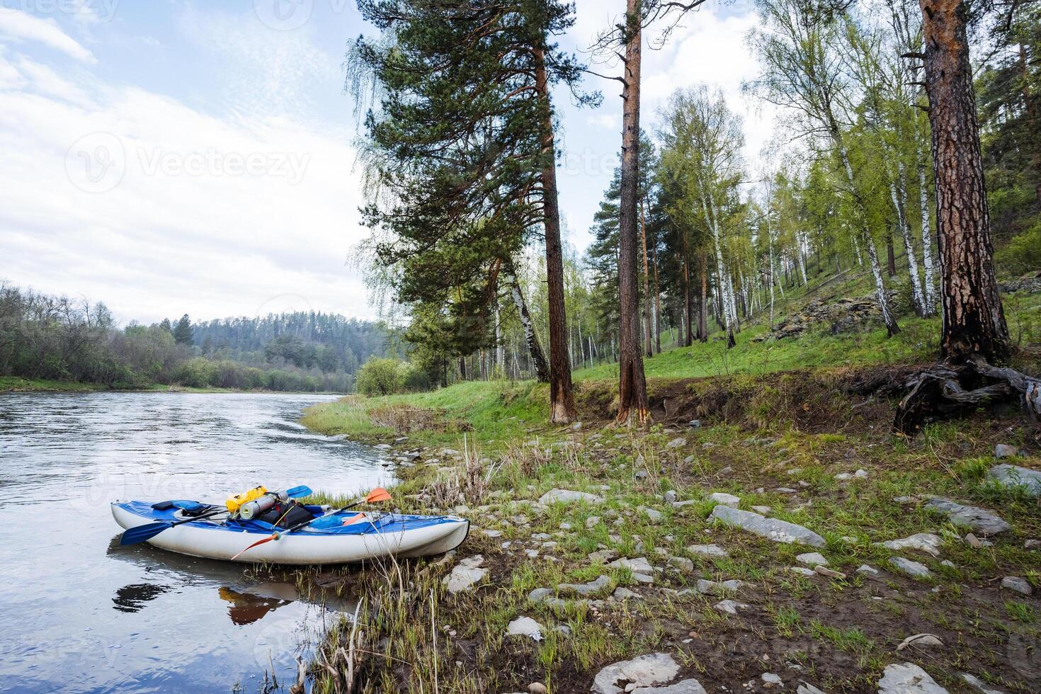 A peaceful, serene riverbank with a kayak floating gently in the water, surrounded by vibrant, lush greenery and trees, offering a tranquil backdrop for adventurous outdoor activities photo