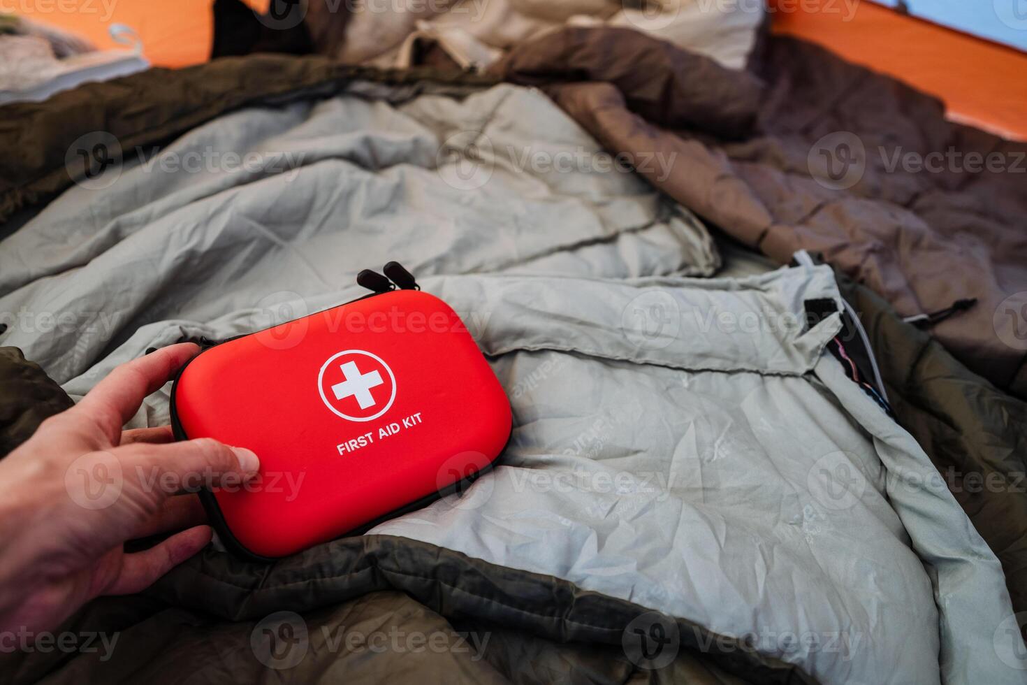 A hand is carefully holding a compact and vibrant red first aid kit against a soft and cozy background of a jacket, which adds a touch of warmth and comfort in the context of adventure photo