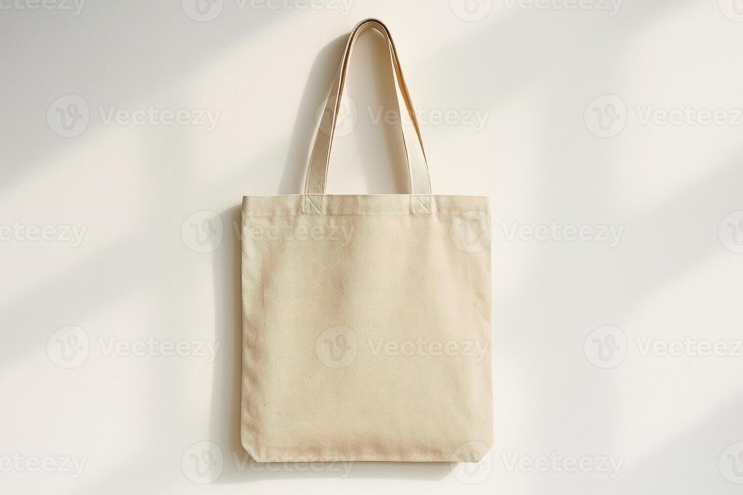 Blank beige canvas tote bag on light wall with soft shadows. Eco-friendly reusable bag mockup with copy space photo