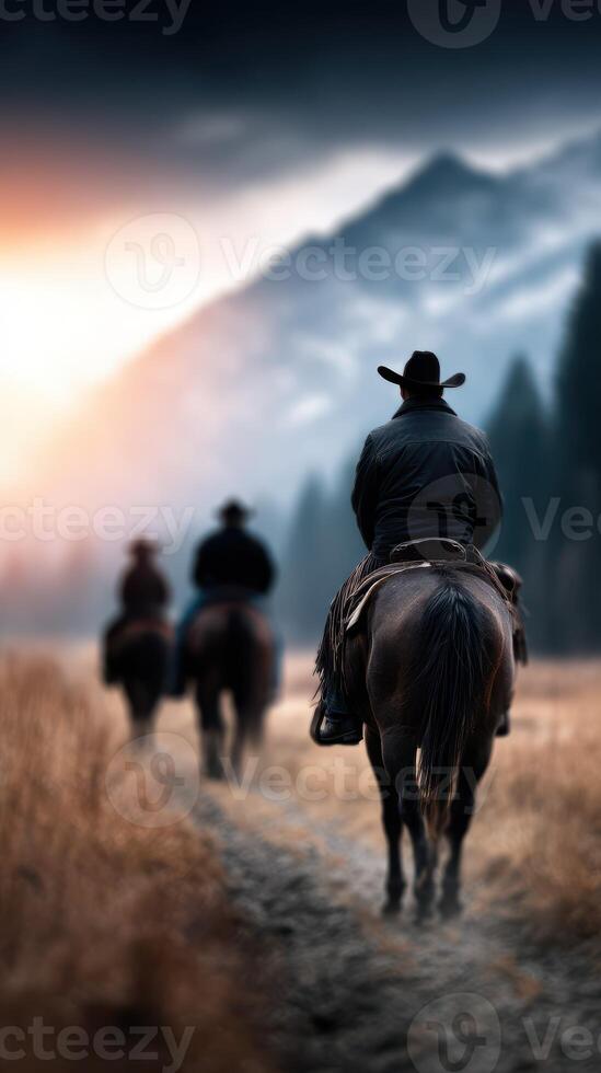 Cowboys ride through a scenic mountain trail at sunset amidst golden grassland and majestic peaks photo