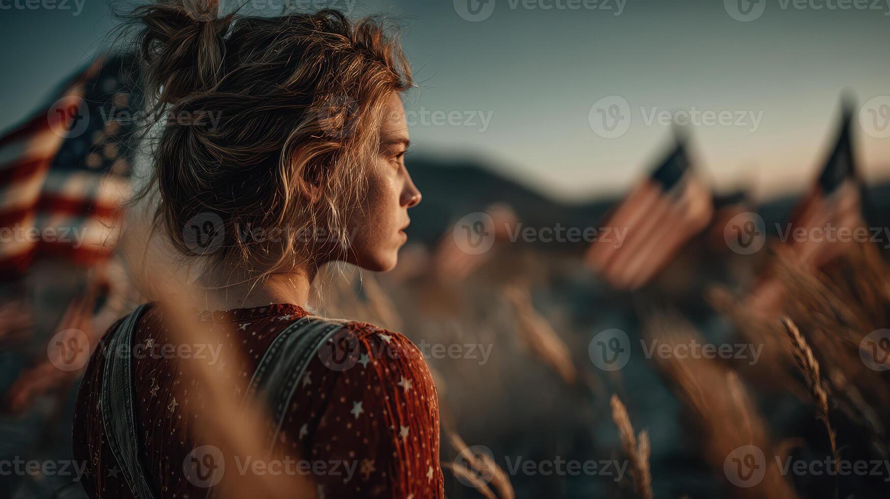 Young woman standing in a field with American flags during sunset reflecting on personal freedom and patriotism photo