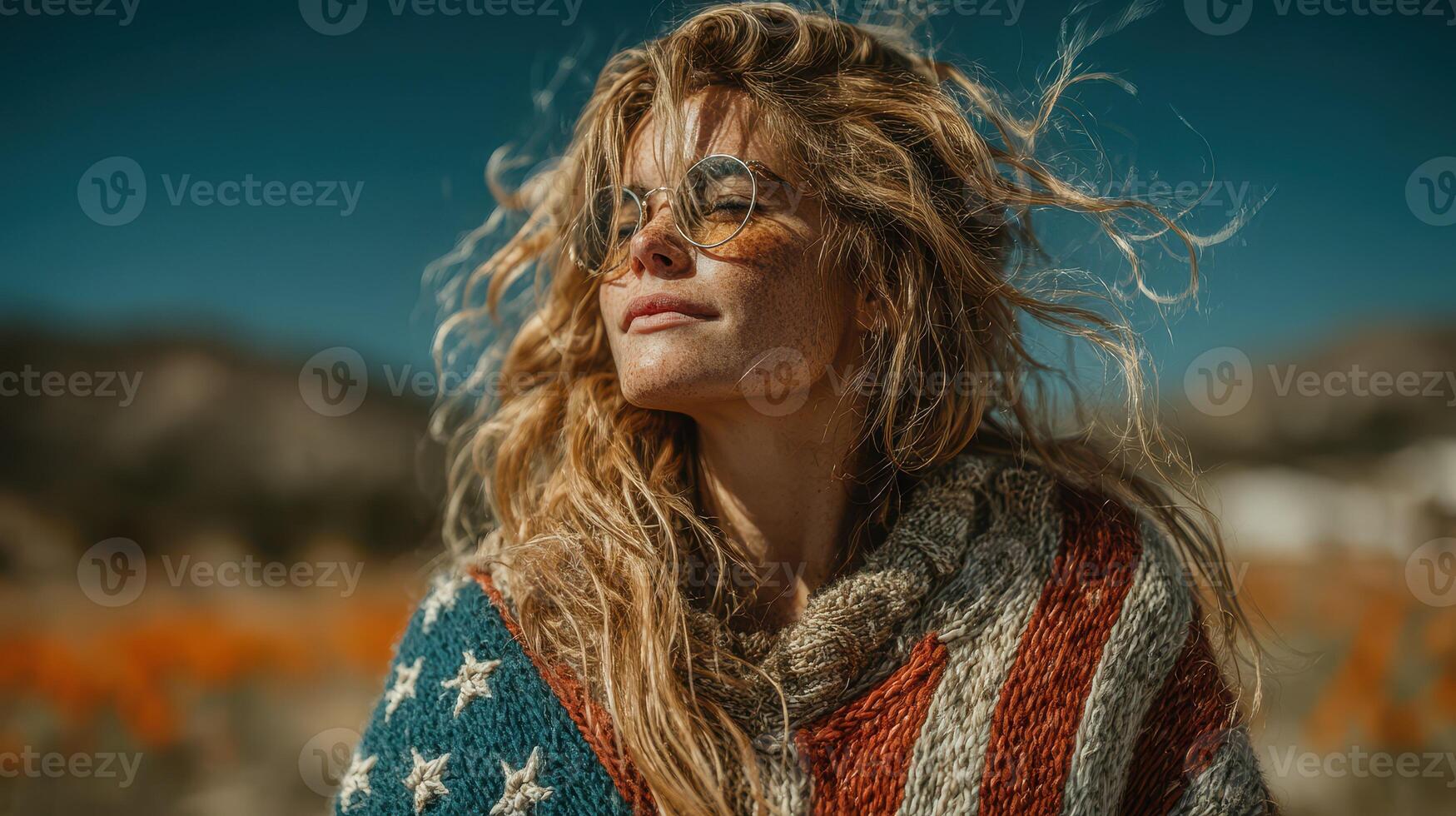 Woman in sunglasses wearing a colorful sweater with stars stands outdoors surrounded by vibrant orange flowers photo