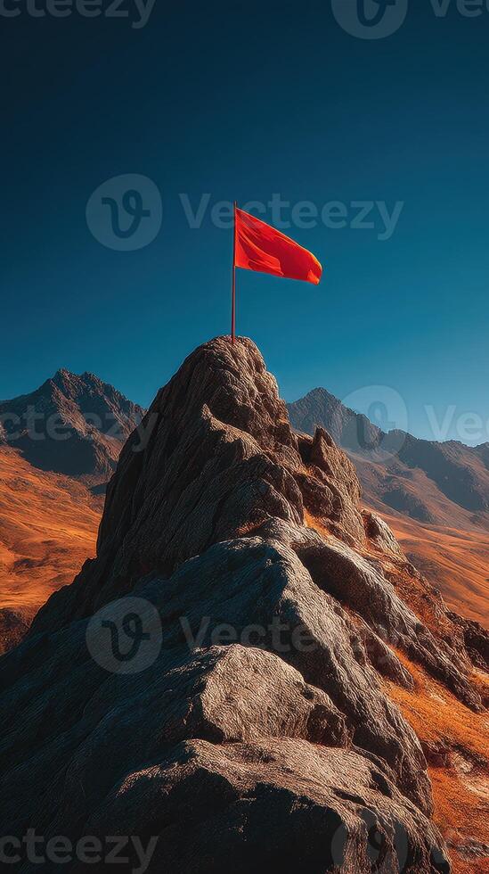 Red flag stands tall on rocky peak against clear blue sky and mountain backdrop during bright daylight hours photo