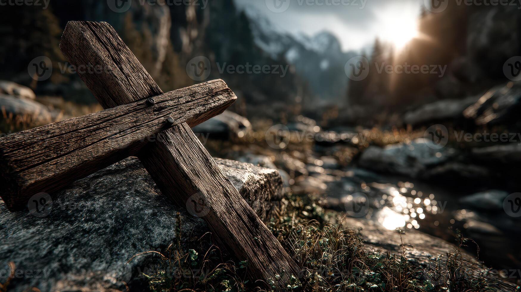Wooden cross rests on rocky ground near a stream at sunset in a serene mountainous landscape photo