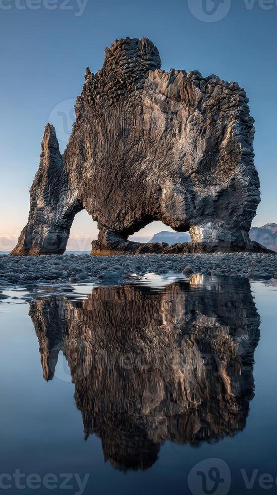 Rocky formation at Hvitserkur beach reflects in tranquil water during sunset, creating a breathtaking natural spectacle photo