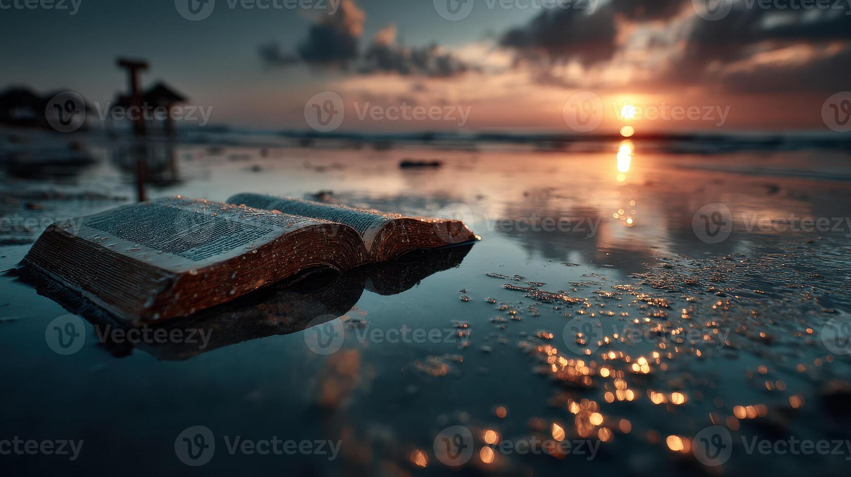 Book left on wet sand at sunset by the beach reflecting colors of the sky in the water photo