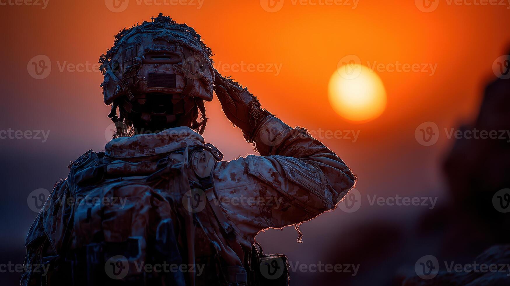 Soldier salutes the setting sun during sunset on a rocky terrain in a desert environment photo