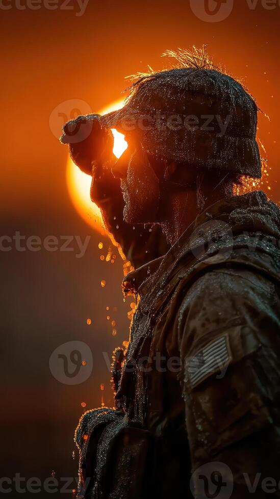 Soldier stands vigilant against backdrop of sunset with water droplets glistening in the fading light photo
