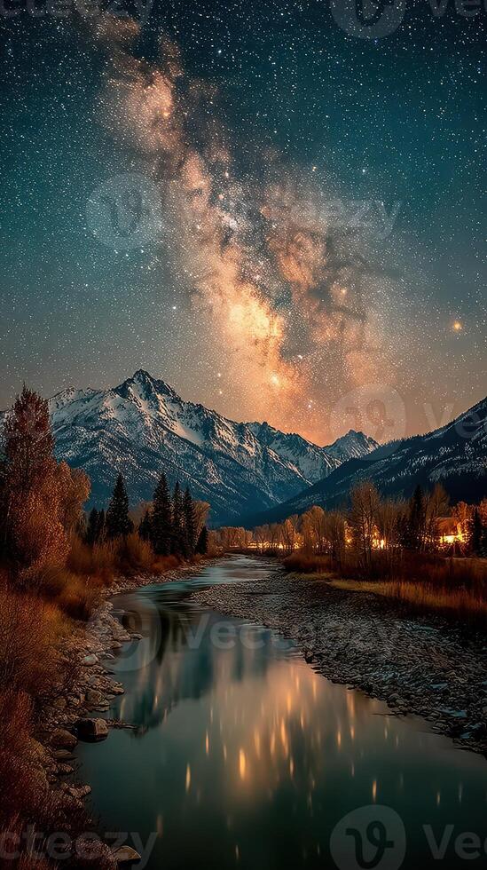 Stars twinkle over a serene river reflecting majestic mountains at night near a peaceful town photo