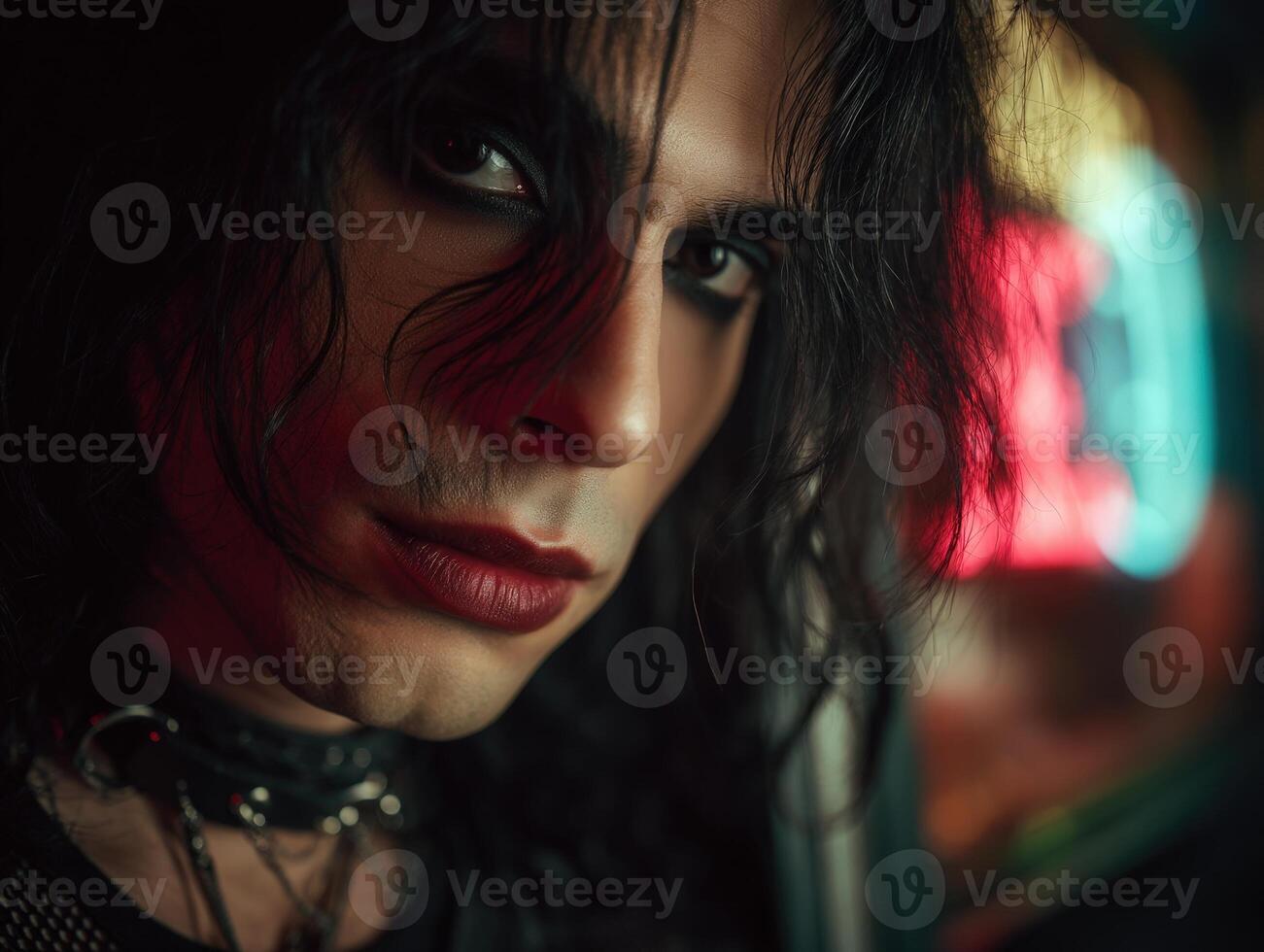 Dark-haired person with intense gaze, smoky eye makeup, and deep red lips, surrounded by blurred neon lights. They wear a choker and have a mysterious, edgy appearance photo