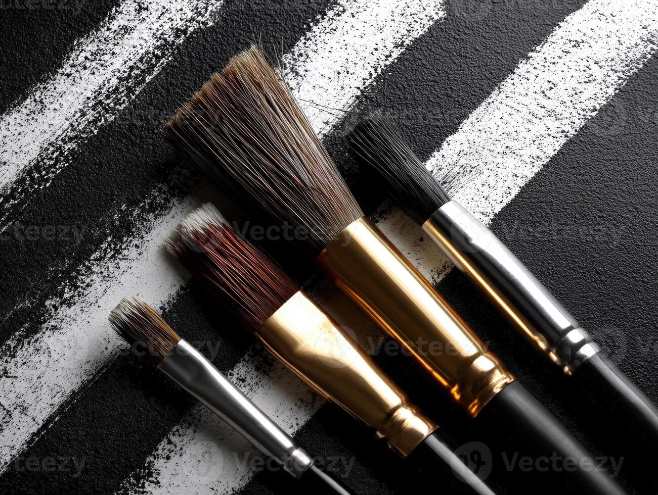 Brushes with metallic ferrules rest over black canvas featuring bold white brushstrokes. Varied bristle sizes suggest use in painting and artistic endeavors, contrasting texture visible photo