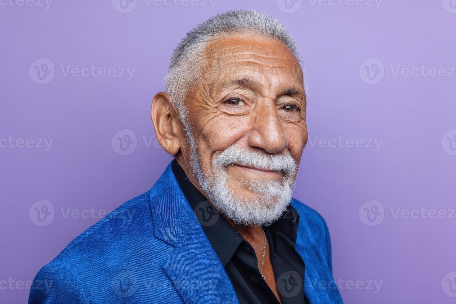 Smiling elderly man with white hair and beard in a vibrant blue jacket over a black shirt, gazing confidently photo