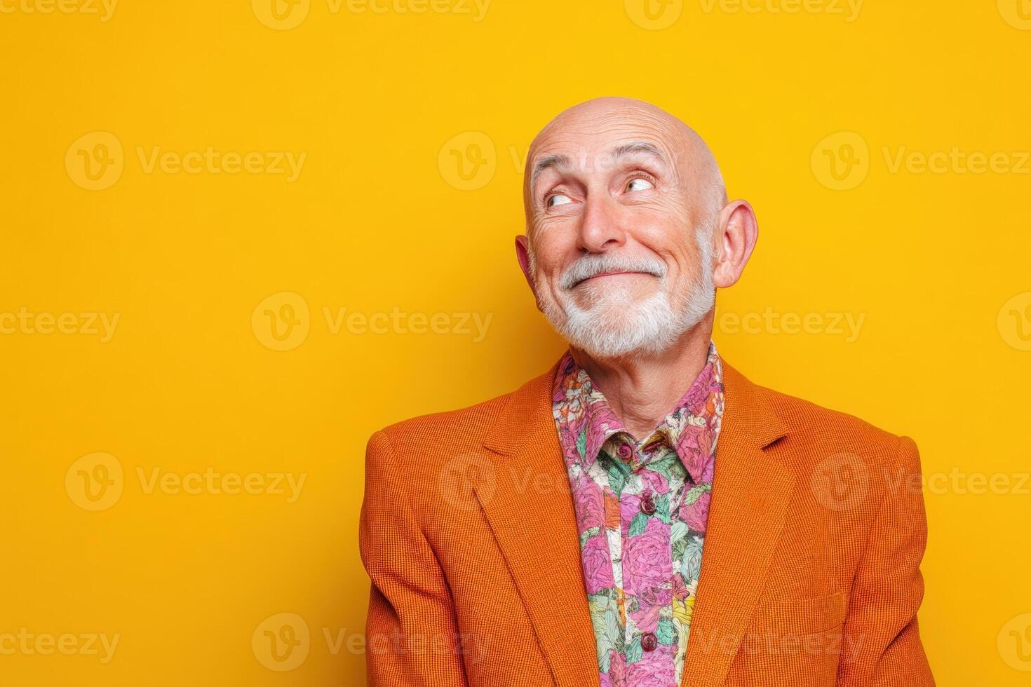 Elderly man with a bald head and white beard, wearing a vibrant orange jacket and a colorful floral shirt, tilts his head slightly, smiling with a thoughtful expression photo