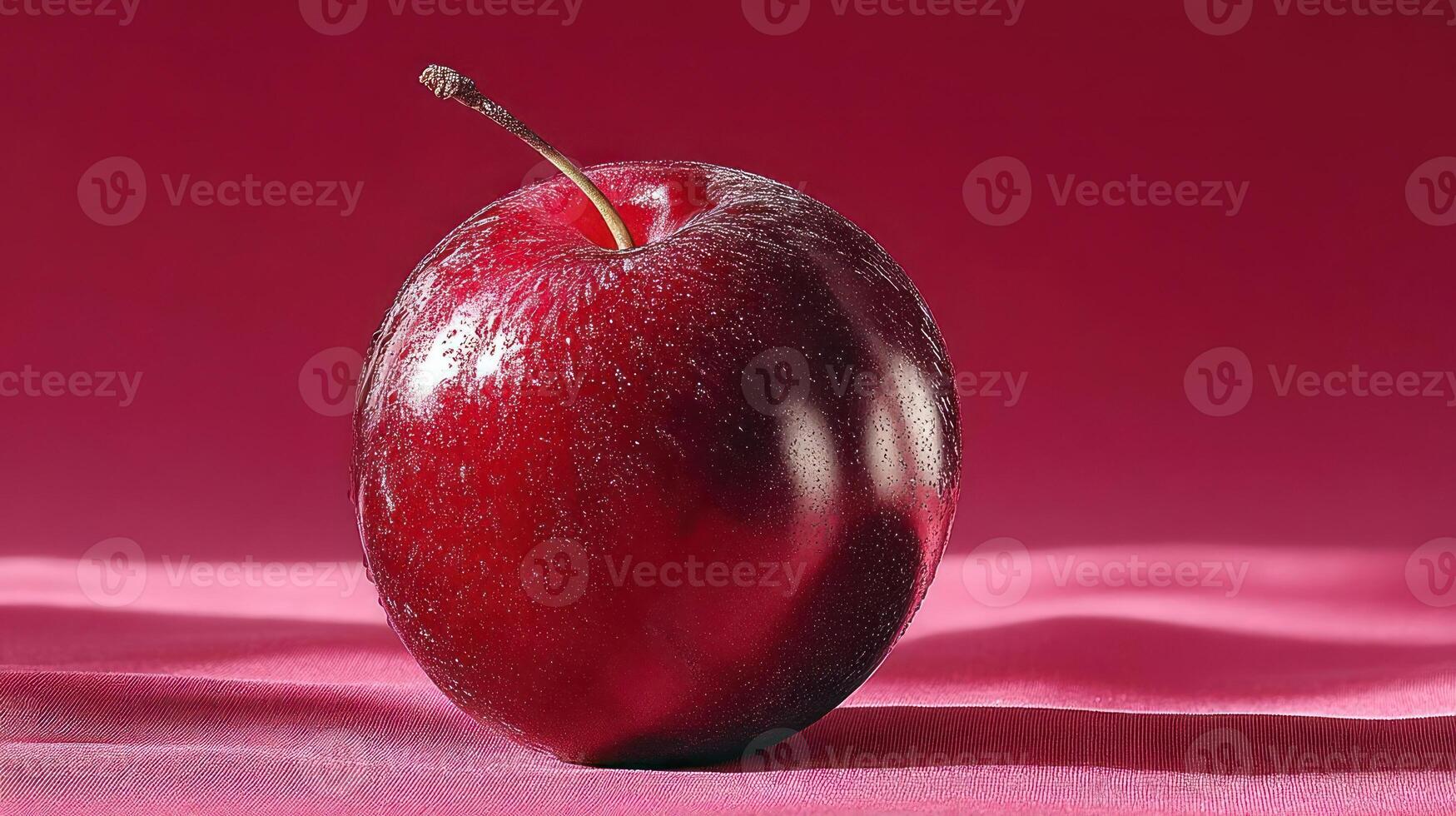 A close-up of a ripe, juicy plum on a pink surface. photo