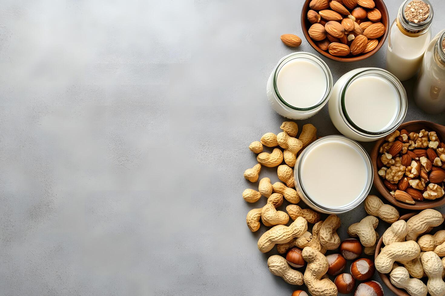 Freshly prepared nut milk alongside bowls with peanuts, almonds and walnuts placed on a gray surface photo
