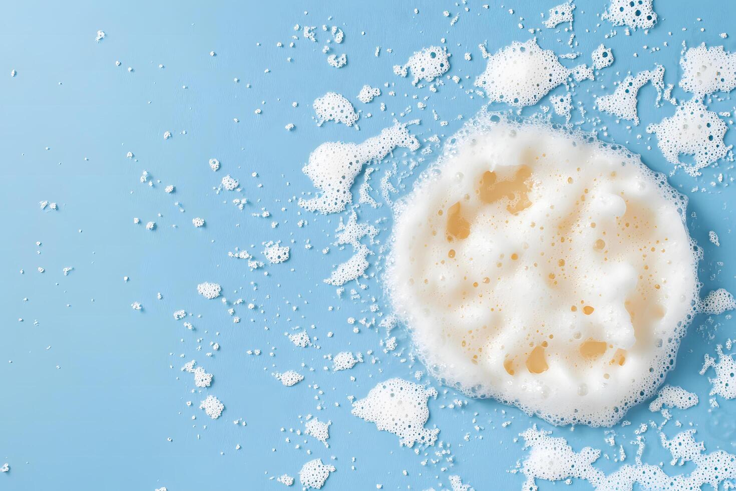 Light blue surface features a circular sponge completely covered in white, foamy soap bubbles photo