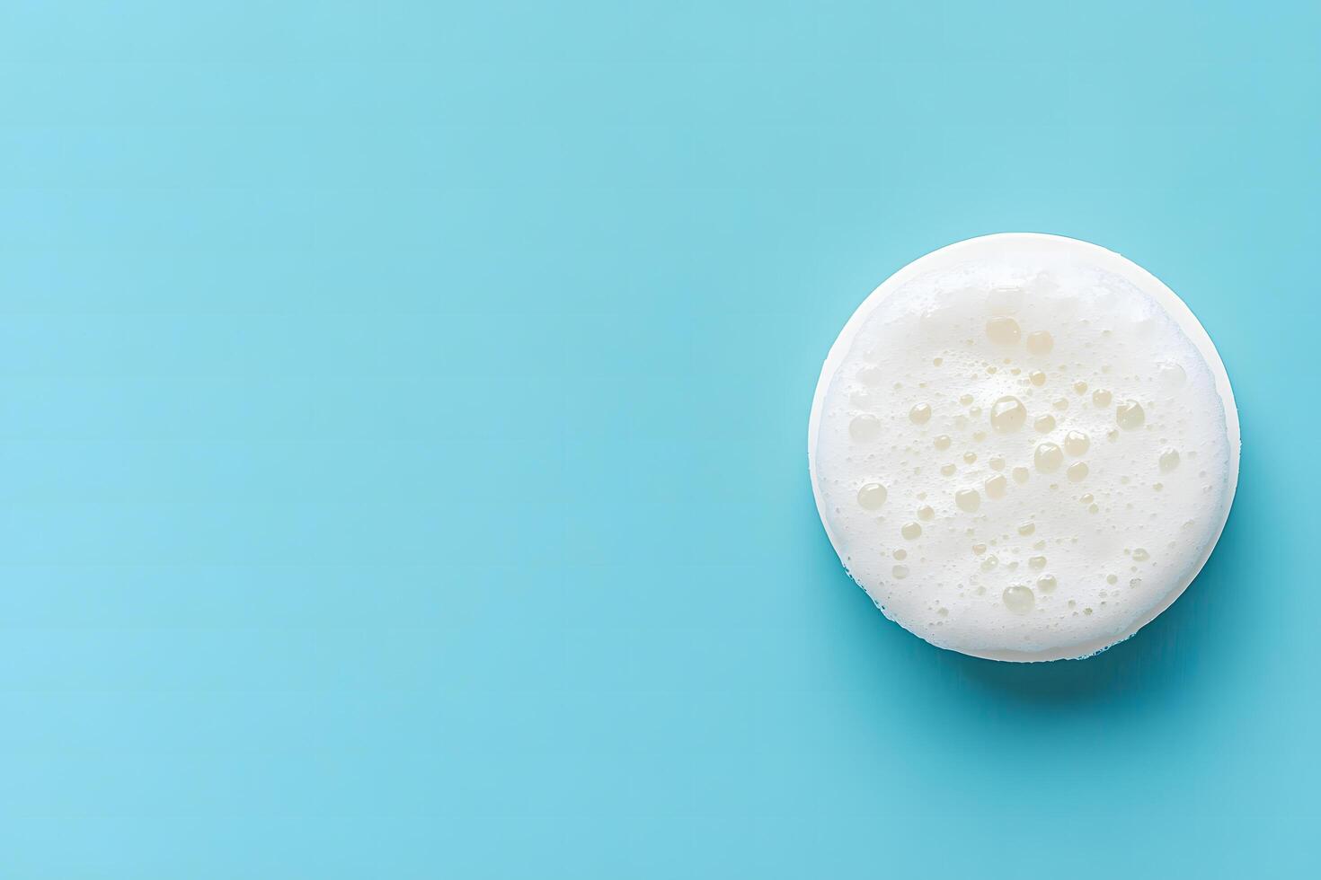 Round white cleansing pad with foamy texture rests against a soft blue background photo