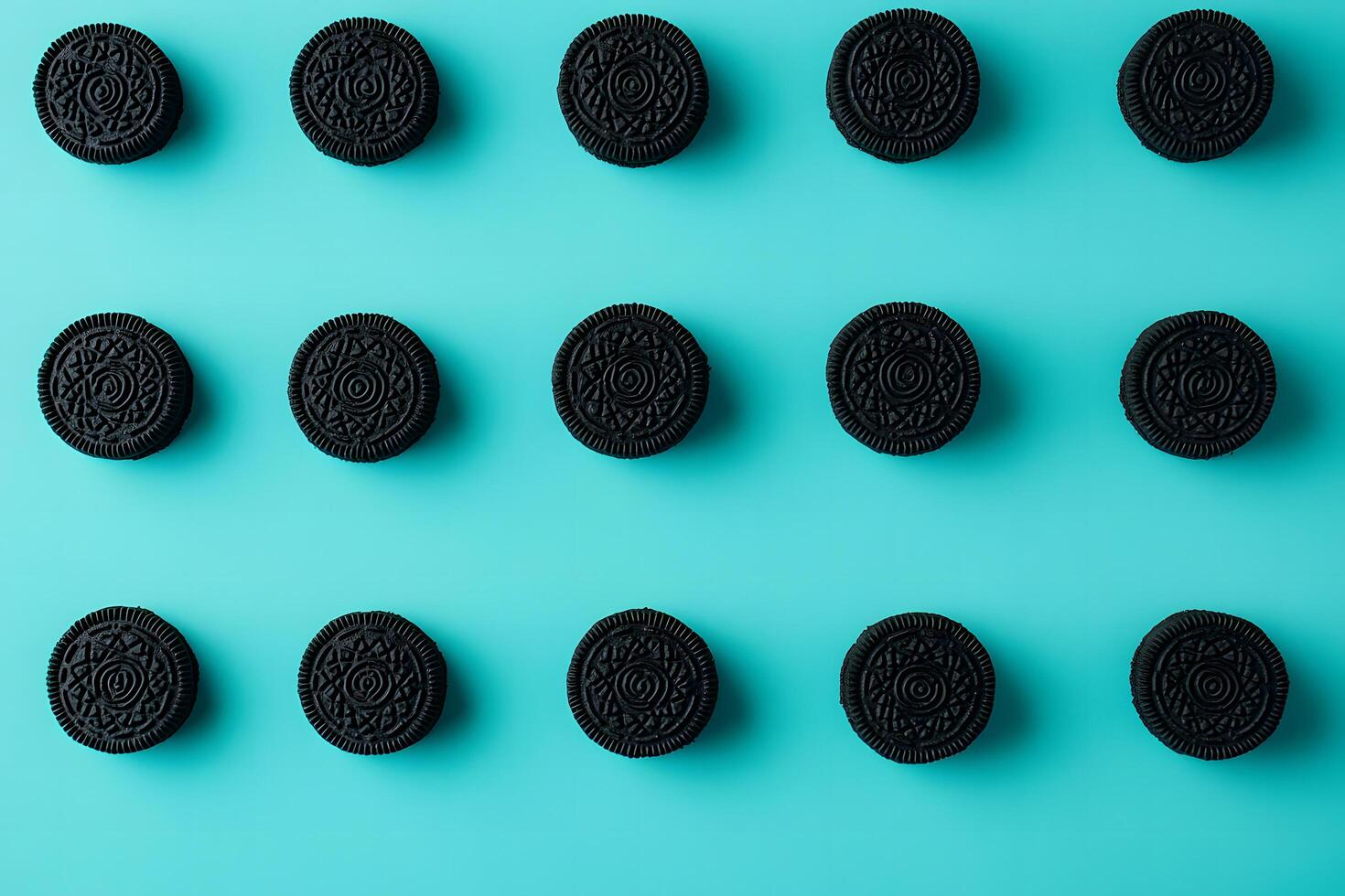Rows of textured black cookies are neatly organized on a vibrant light blue backdrop photo