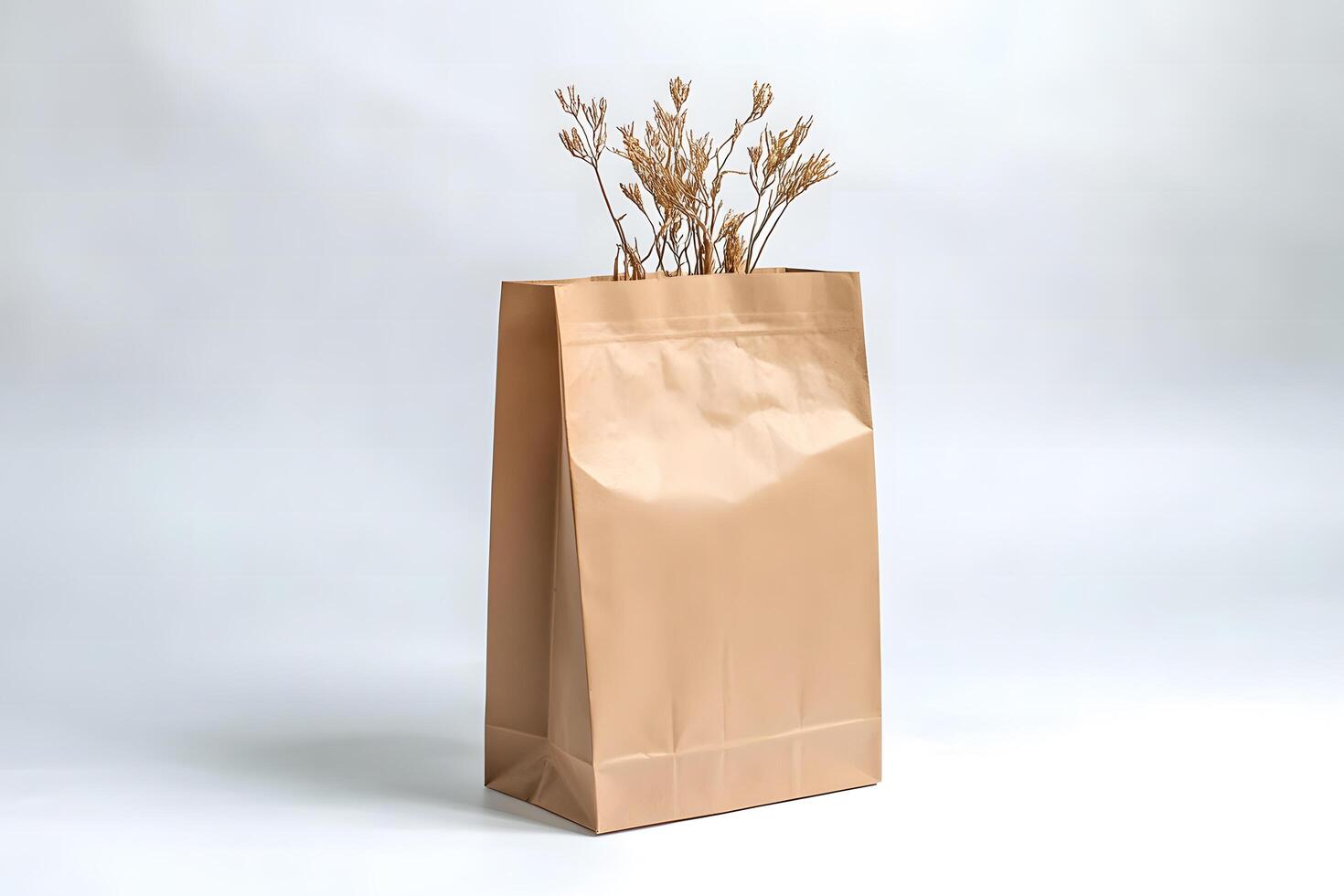 Still life depicts dried floral twigs emerging from a shiny tan paper bag photo