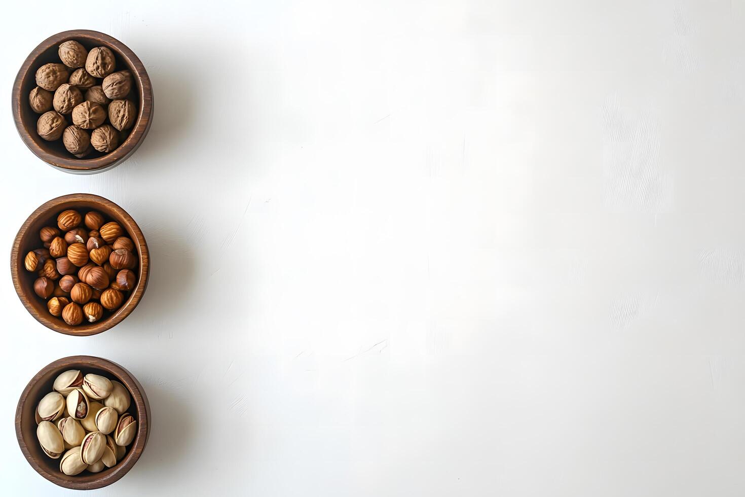 Three wooden bowls hold walnuts, hazelnuts, and pistachios, positioned vertically on a white background photo