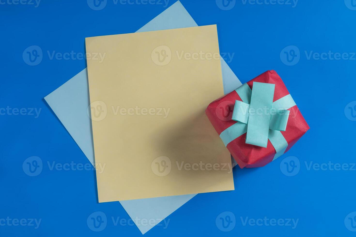 Red gift box with a blue ribbon and papers on a blue background. photo
