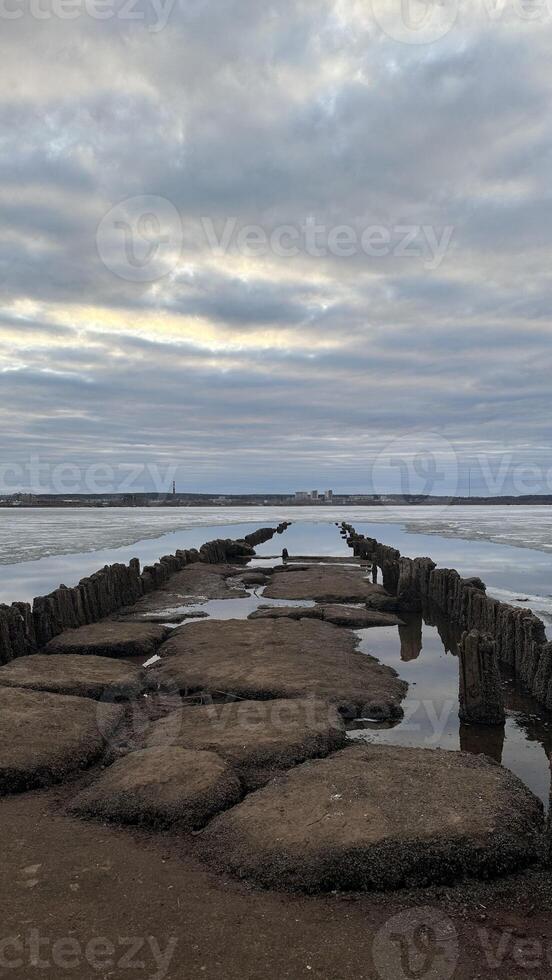 An old wooden destroyed bridge on a frozen river, spring ice melting on the river. photo