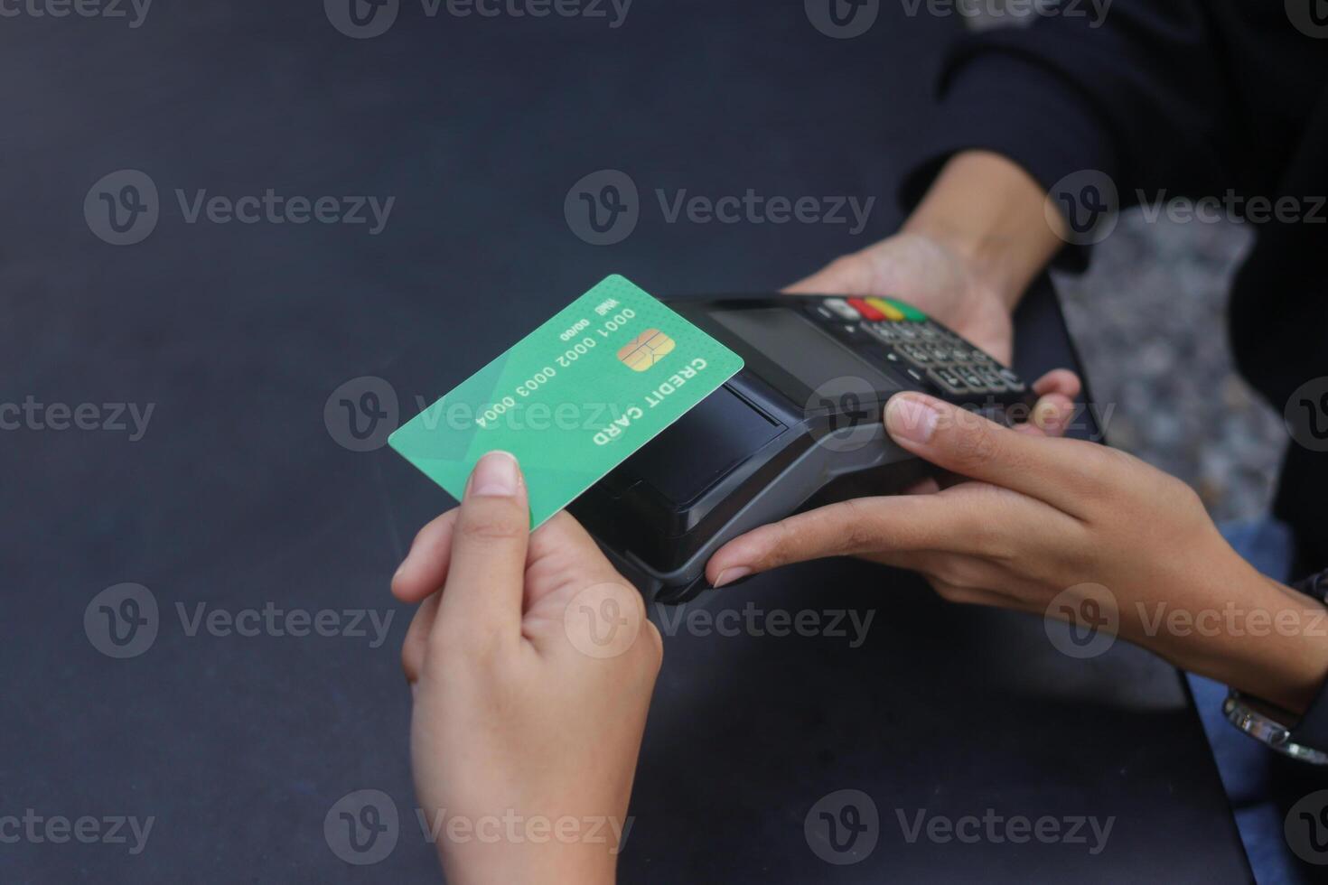Close up of credit card payment using a point of sale terminal. Close-up of hand swiping a green card while another person waits at a table. Modern cashless transaction concept. photo