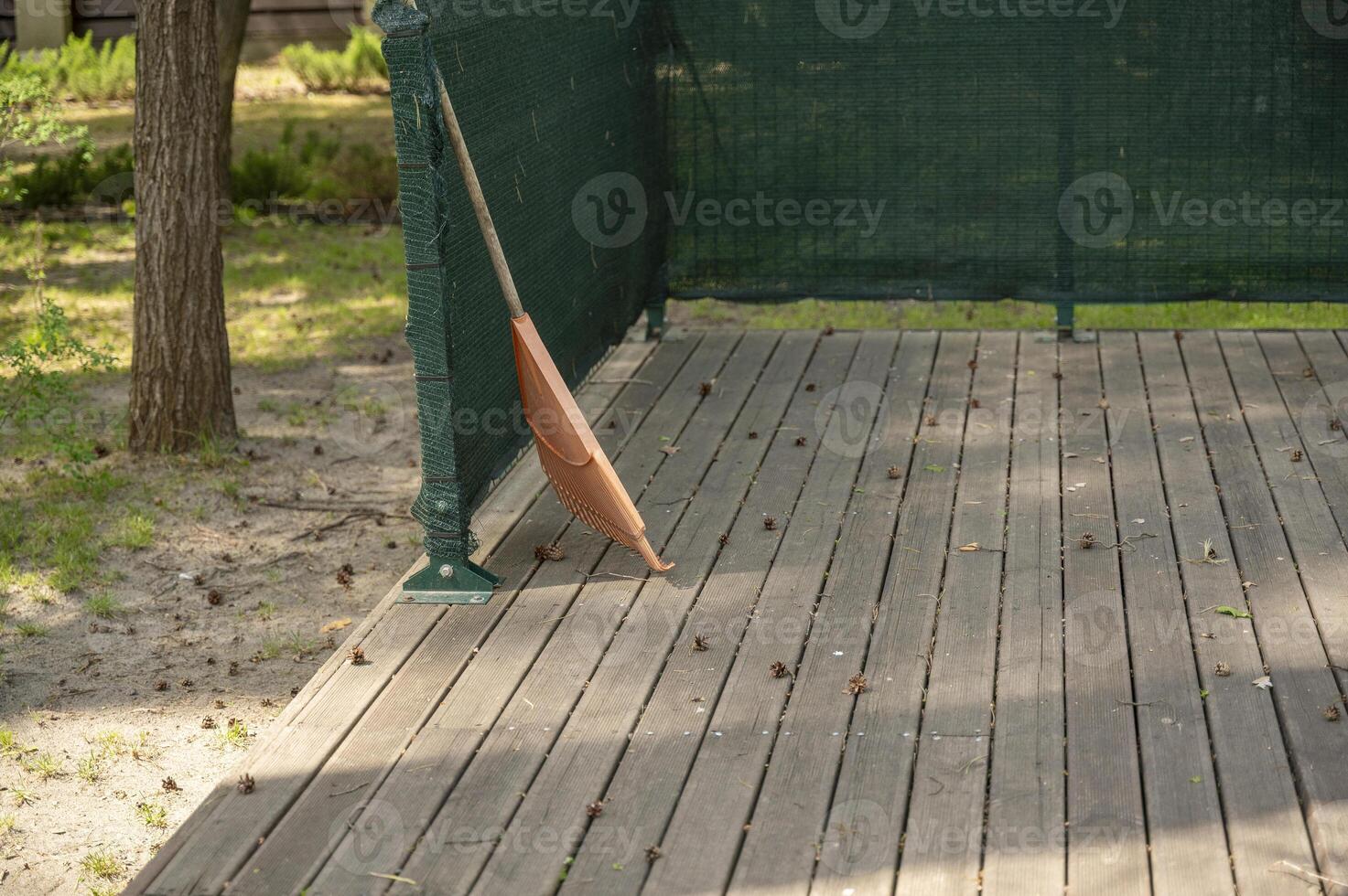 orange rake on a wooden platform, against the background of a park. pine cones are lying on a wooden platform. photo