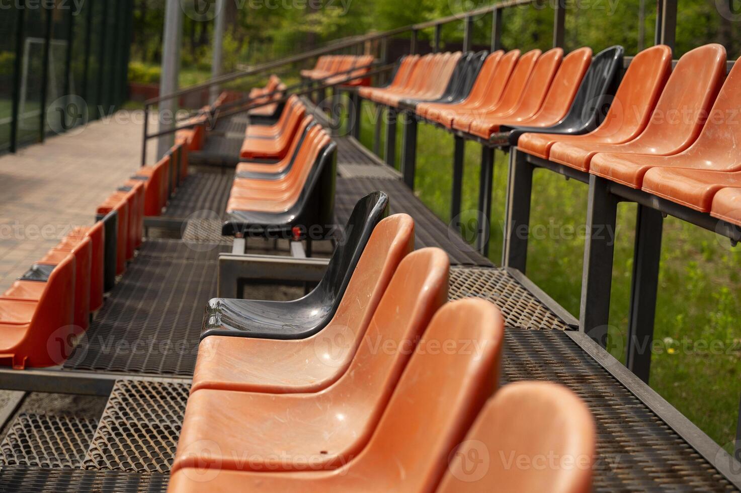 Close-up of Rows of empty orange and black plastic seats on the grandstand outside an outdoor sports stadium. stretching into the distance. High quality photo